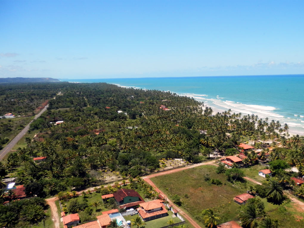 Vista aérea do empreendimento à beira-mar, com ruas pavimentadas e vegetação preservada